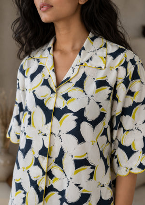 
                  
                    Woman wearing a floral patterned shirt with white flowers and yellow accents on a dark background.
                  
                