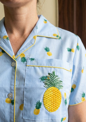 
                  
                    Light blue shirt with pineapple patterns worn by a person
                  
                