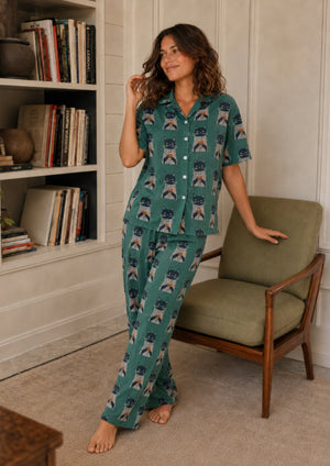
                  
                    Woman wearing a green pajama set with cat pattern in a room with a bookshelf and chair.
                  
                