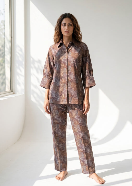 Woman wearing a patterned pajama set in a bright room with sunlight filtering through.