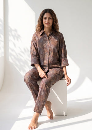 
                  
                    Woman wearing a brown patterned outfit sitting on a white surface with a white background
                  
                