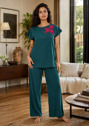
                  
                    Woman wearing teal pajama set with floral embroidery in a living room.
                  
                